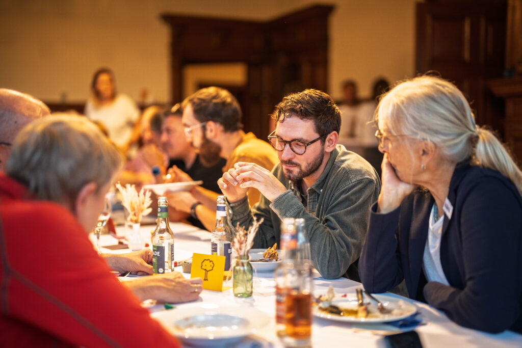 Mehrere Personen sitzen an einem langen Tisch und essen gemeinsam in einem warm beleuchteten Raum