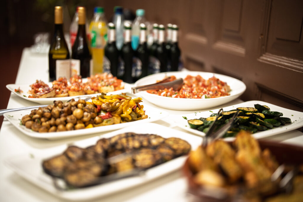 Buffet mit verschiedenen warmen und kalten Speisen auf weißen Tellern und mehreren Flaschen im Hintergrund