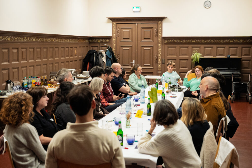Menschen sitzen an einem langen Tisch in einem Raum mit Holzvertäfelung und unterhalten sich