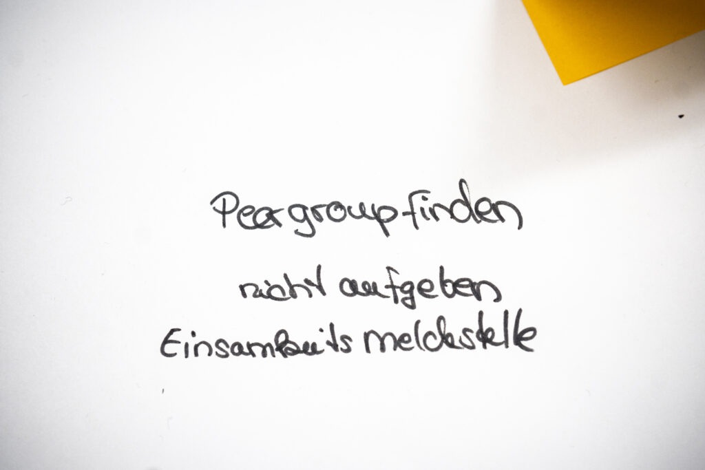 Handschriftliche Notiz mit den Worten 'Peer group finden', 'nicht aufgeben' und 'Einsamkeitsmeldestelle' auf weißem Papier