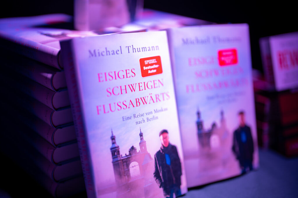 Bücherstapel mit dem Buch 'Eisiges Schweigen Flussabwärts' von Michael Thumann, Vorderseite zeigt eine Person vor einem historischen Torbogen.